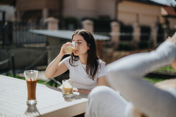 A young woman drinks an iced coffee outdoors in a relaxed, sunny setting, highlighting casual interaction and focus on refreshment and relaxation during leisure time.