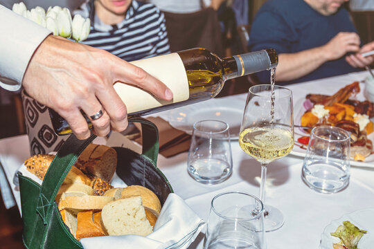 Waiter pouring white wine into glass at upscale formal dinner restaurant