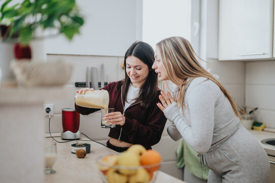 Women in casual attire making a smoothie together in a kitchen. Warm and collaborative atmosphere is expressed as they enjoy cooking and preparing healthy food together, fostering a joyful connection.