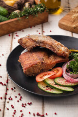 Crispy fried fish served with sliced tomatoes, cucumbers, onions and fresh herbs on a black plate