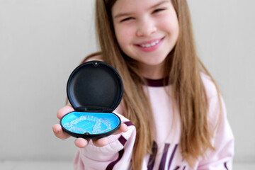 Smiling girl holding case with clear dental aligners, showing modern orthodontic care and teen dental hygiene. Close up lifestyle shot perfect for ads about aligners, dentistry, healthy teeth habits