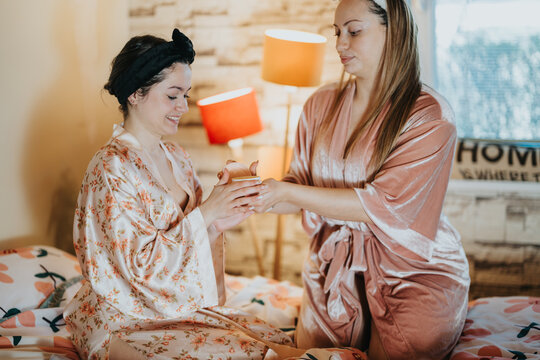 Two women wearing soft robes enjoy a calm moment together indoors, suggesting warmth and relaxation. This image emphasizes friendship, comfort, and serene connectivity in a home environment.