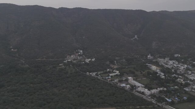 Aerial shot of Jamini Kund Road in Pushkar featuring a dramatic cloudy sky over the Aravali hills and the townscape below, capturing the calm evening atmosphere and the scenic landscape from above.