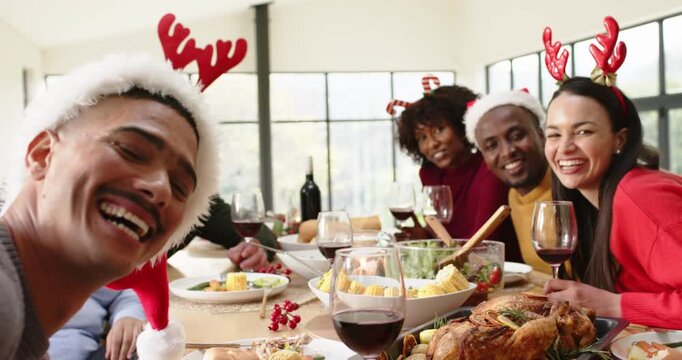 Diverse friends in antlers taking selfie, turning toward camera and toasting at table