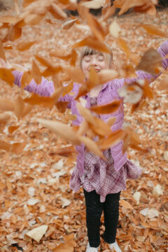 Young girl playing outdoors throwing autumn leaves