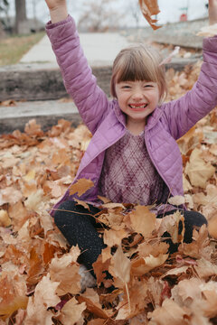 Happy girl playing, throwing autumn leaves in park