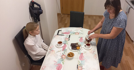 Woman serving tea and cookies to girl at dining table indoors