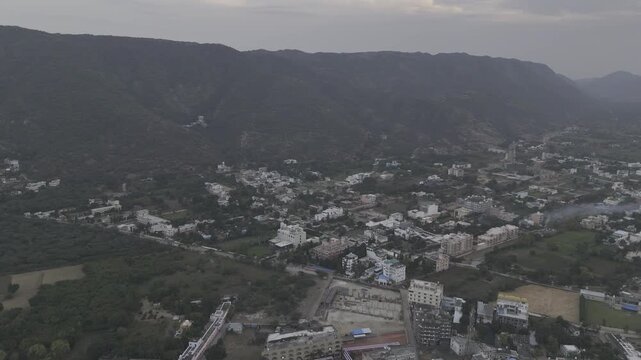 Aerial view of Pushkar town near the Gurudwara during evening, with clustered houses and streets in the foreground and lush green Aravali mountains forming a scenic backdrop under soft evening light.