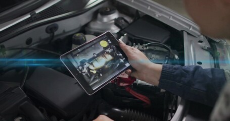 Holding tablet, technician in work jacket showing engine map over open car hood with red cable