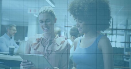 Holding tablet, two colleagues reviewing content in modern office in ruffled blouse and blue top