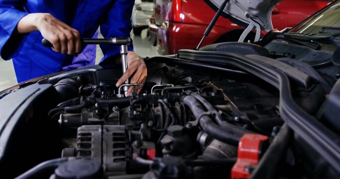 Tightening woman mechanic in blue coveralls using socket wrench on engine bay in shop, red terminal - Powered by Adobe