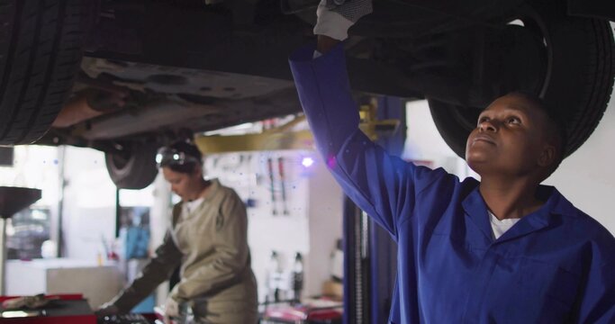 Inspecting technician in blue coveralls reaching under raised car at shop bay, tools, copy space