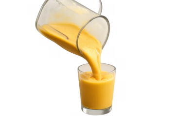 Pouring fresh yellow fruit smoothie from a blender pitcher into a glass, preparing a healthy liquid drink