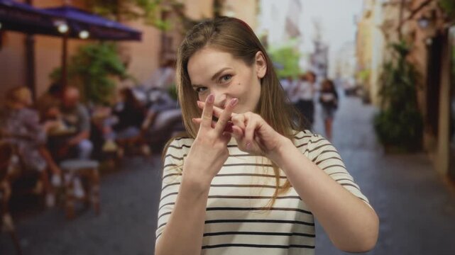 Woman crossing index fingers in front of her on a busy street terrace by cafe tables under umbrellas with a playful smile; rejection.