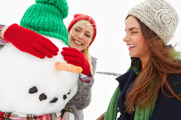 Women, friends and building snowman with eyes, coal and outdoor for bonding, fun or winter holiday....