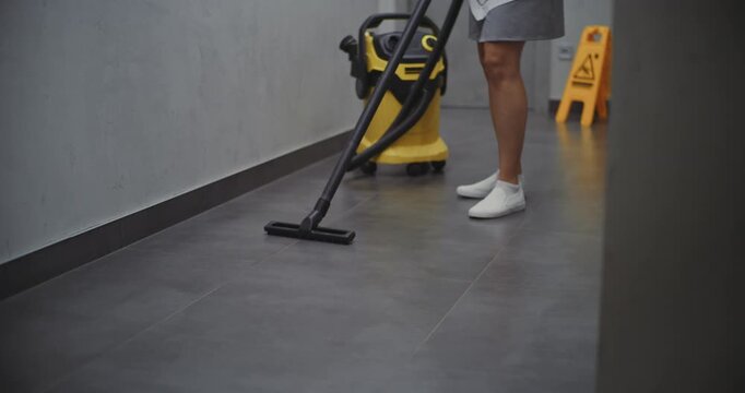 Female Cleaning Staff Vacuuming Floor in Hotel Corridor. Housekeeper in Grey Uniform Carefully Tidies Hallway, Keeping Common Areas Neat and Welcoming for Guests. Professional Housekeeping Routine.