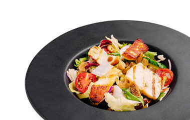 Grilled chicken salad served on a black plate with fresh vegetables