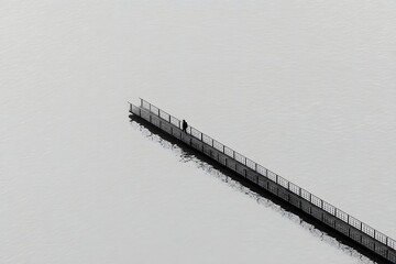 Solitary figure walking along a pier stretching out into the calm water of a large lake