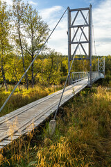 Wooden deck of the suspension bridge across the calm autumnal river, hiking and backpacking trail in Sweden