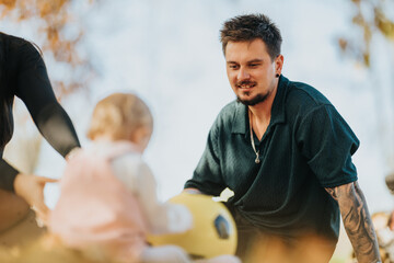 A man with a tattooed arm assists a young child on a bicycle helmet in a sunlit autumn park, capturing a moment of family bonding and outdoor activity.