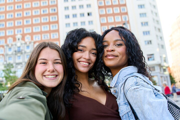 Three young women smiling together in a city center