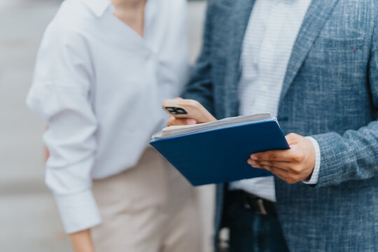 Two colleagues collaboratively working outdoors, examining documents, and using a smartphone for organization. - Powered by Adobe