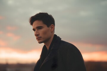 Thoughtful man gazes at the horizon during sunset with dramatic clouds in the background