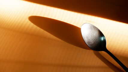 Stainless spoon placed at the angle with diagonal shadow reflection during summer. Close-up spoon and ray of light texture. Still-life, abstract, kitchenware, minimal concept for background, print.