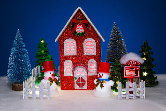 A red house with Christmas trees and snowmen surrounded by a fence