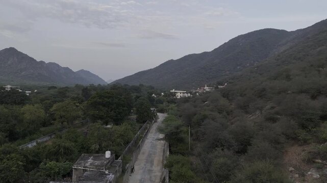 Aerial shot of Jamini Kund Road in Pushkar featuring a dramatic cloudy sky over the Aravali hills and the townscape below, capturing the calm evening atmosphere and the scenic landscape from above.