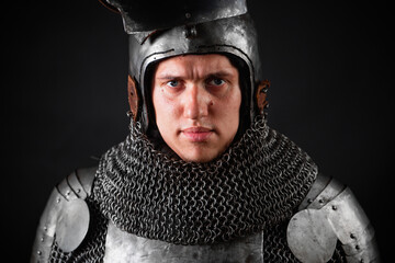 Close-up portrait of a medieval knight in full plate armor and helmet with raised visor isolated on dark background.