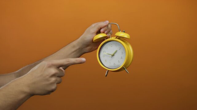 Man hand holding yellow clock against orange wall vividly showing time management emphasis.