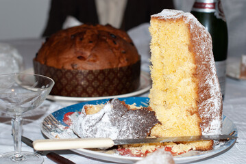 A sliced pandoro dusted with powdered sugar sits on a festive plate beside a whole panettone, capturing a classic holiday dessert scene perfect for Christmas celebrations.