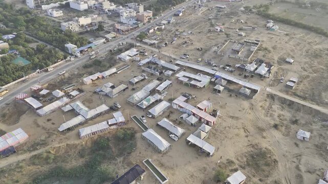 Aerial shot of a pond near Pushkar cattle fair ground with horse tents, captured at sunrise with Aravalli mountains in the background.
