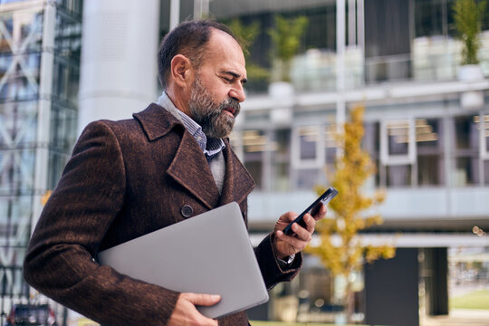 Professional Man Using Smartphone in City, Carrying Laptop in Autumn Business Setting