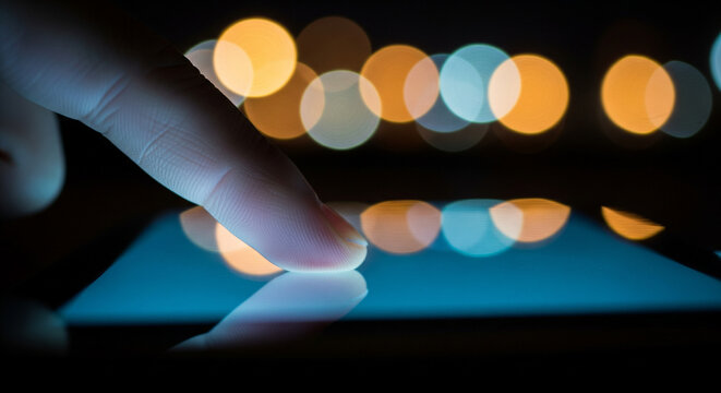 A person's finger touching a glowing smartphone screen at night with a vibrant city lights bokeh background - Powered by Adobe