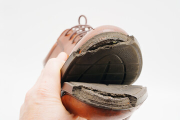 Worn out shoes held in hand showcasing damaged sole