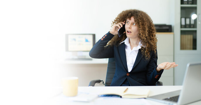 Confused businesswoman talking on phone at modern office desk with documents