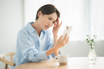 考えながらスマートフォンを見ている日本人女性