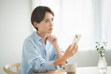 リビングでスマートフォンを持ち考えている日本人女性