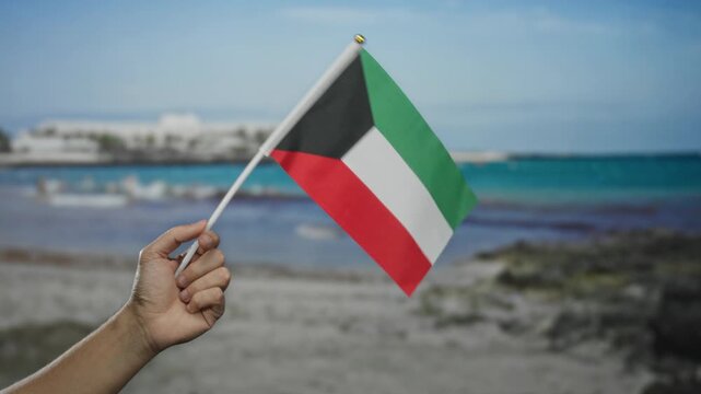 Man holding kuwaiti flag at seaside beach, showcasing national pride and cultural identity in outdoor setting under clear blue sky.