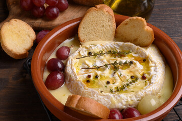 Baked camembert or  brie cheese with honey, grapes, aromatic herbs and crusty bread