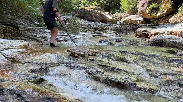 Gold panning in a mountain creek, search for gold in summer. Man is looking for gold with a metal detector. Outdoor adventures on river