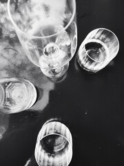 White transparent glasses on a black background. An array of clear glassware is arranged on a dark, reflective surface. The unique angles and reflections create an abstract composition.