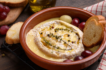 Baked camembert or  brie cheese with honey, grapes, aromatic herbs and crusty bread