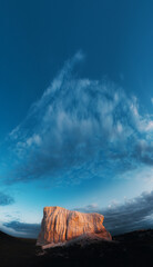 Majestic sandstone formation under dramatic blue sky with clouds at sunset