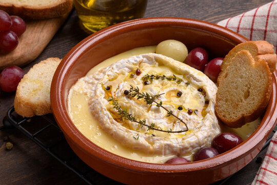Baked camembert or  brie cheese with honey, grapes, aromatic herbs and crusty bread