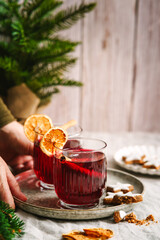 Eine Frau h&auml;lt ein Serviertablett mit zwei Gl&auml;ser Gl&uuml;hwein auf einem Leinen Tischtuch. Alkoholisches Getr&auml;nk, Weihnachten. 