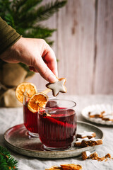 Eine Frau h&auml;lt einen Zimtstere Keks &uuml;ber einem Glas Gl&uuml;hwein. Hei&szlig;getr&auml;nk, Alkohol, Weihnachten. 