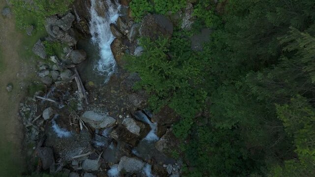 Top-down view of a clear mountain creek flowing through the valley - overcast early summer (June), fresh green vegetation and big weathered boulders around a shallow, crystalline channel